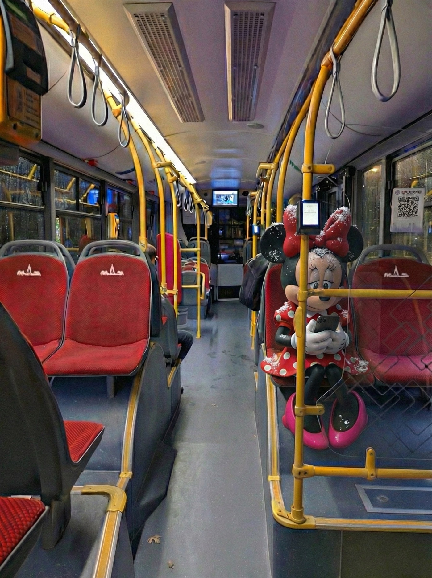 Пустой автобус, грустная Минни сидит на сидении и смотрит в телефон.