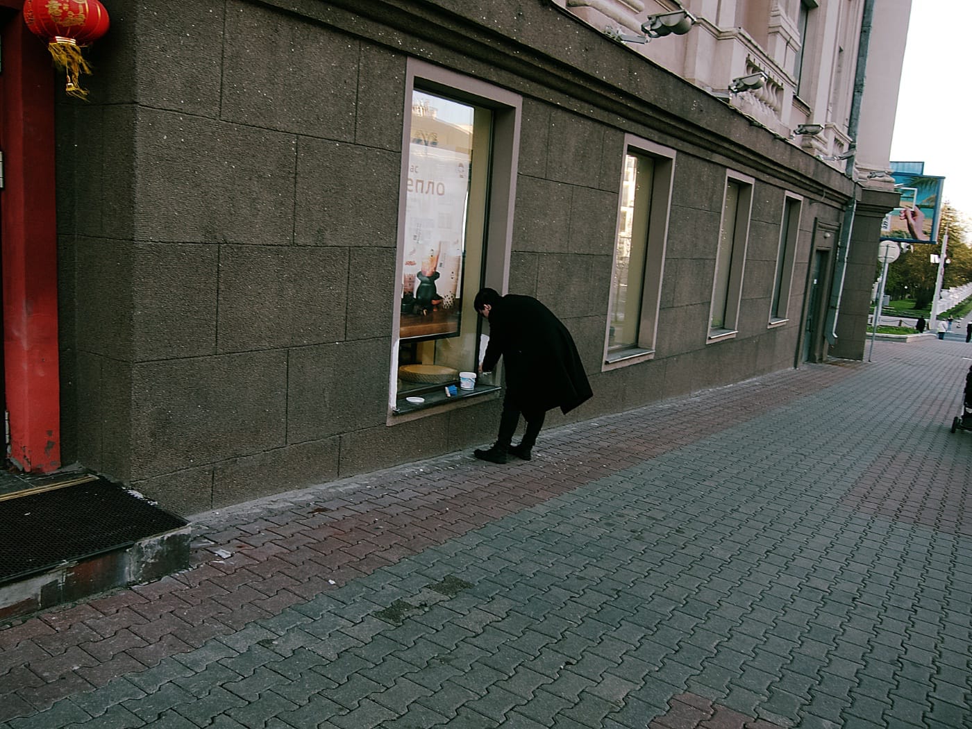 Мужчина в чёрном красит фасад кафе в центре Минска