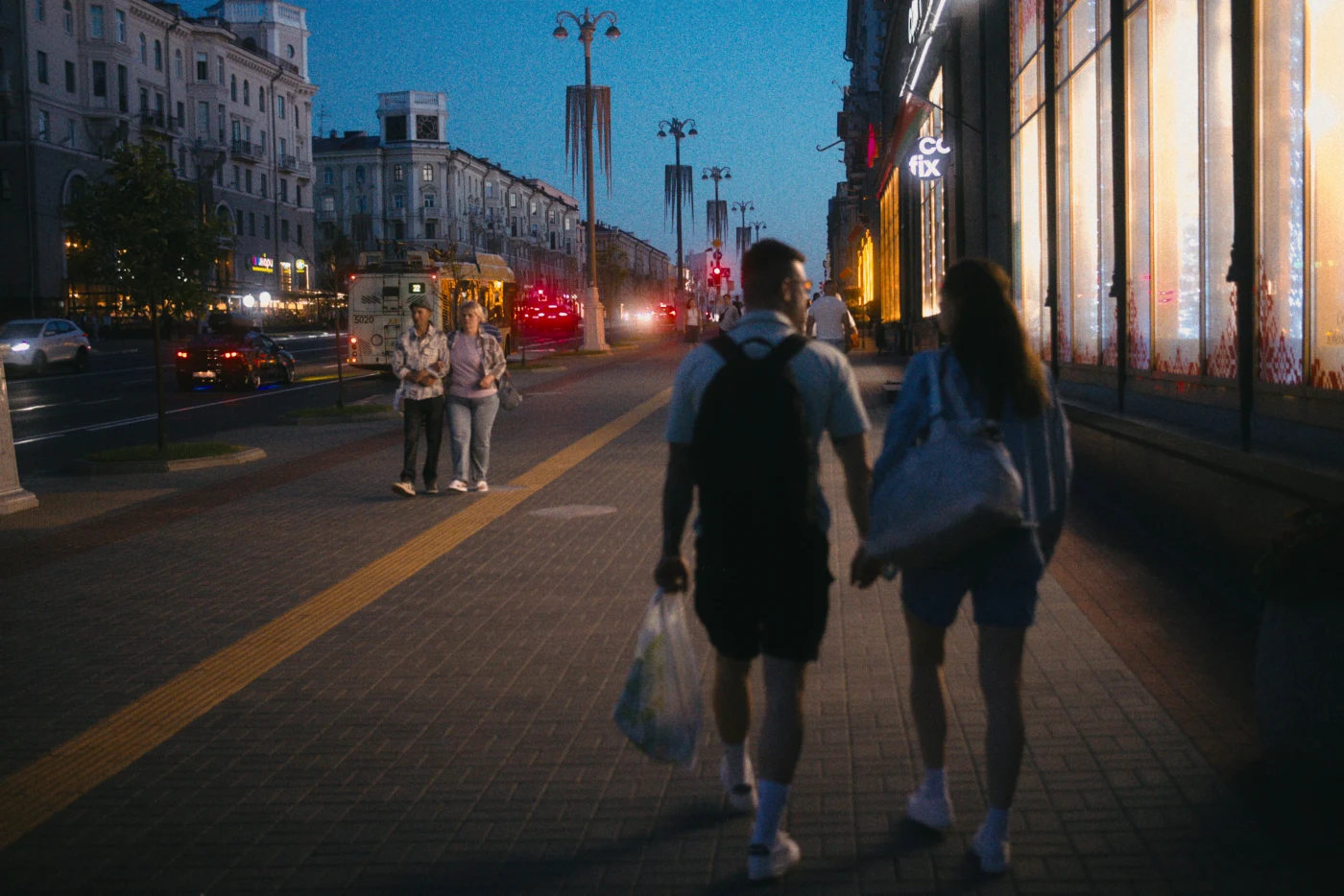 Пара гуляет по вечернему городу, мимо витрин и людей, освещенных огнями.
