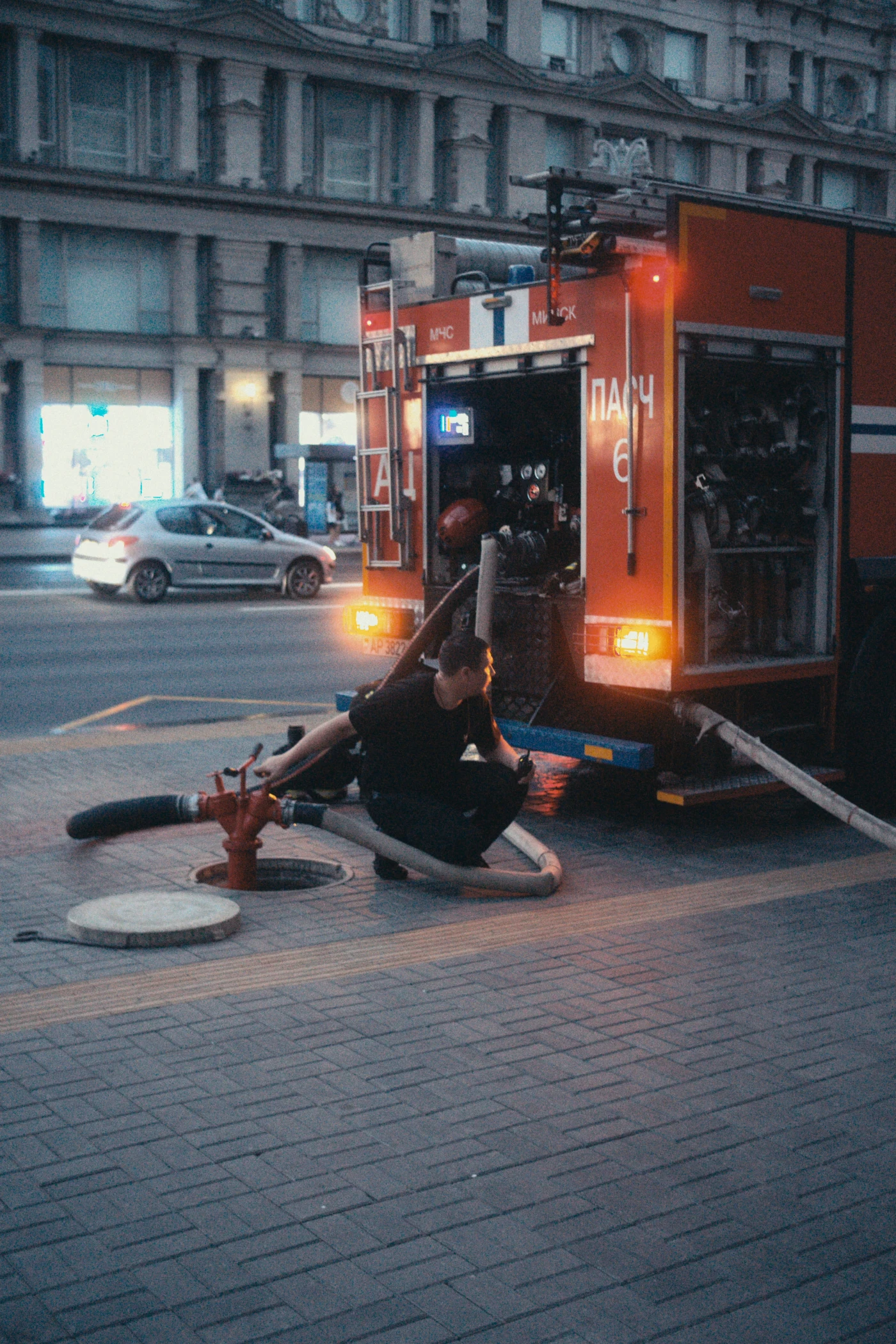 A fire truck connected to a hydrant, while a firefighter checks equipment on the street.