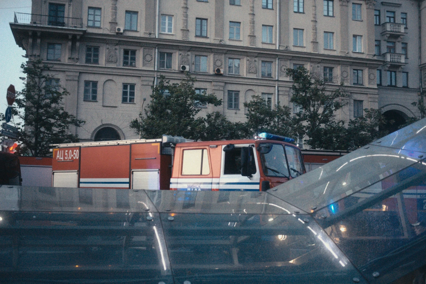 A fire truck against the backdrop of a building, with trees and a glass structure in the foreground.