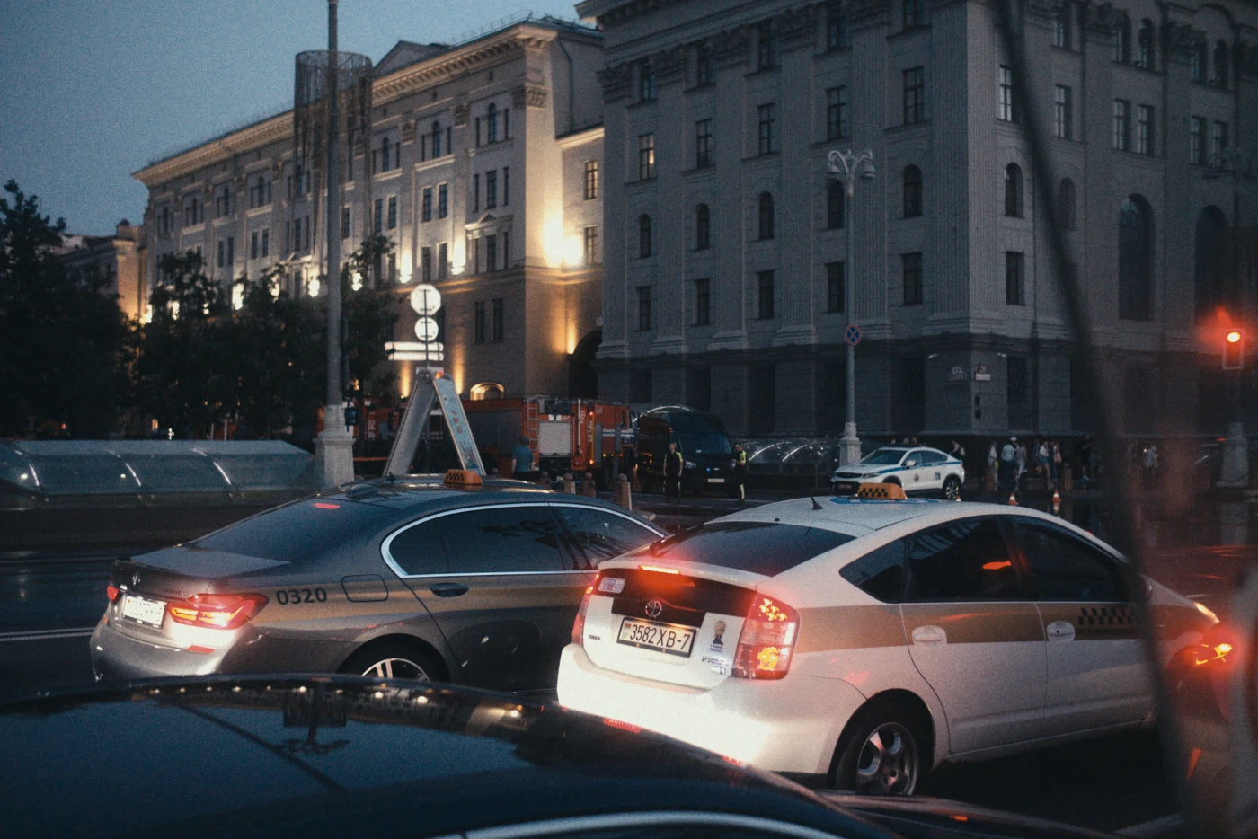 A nighttime cityscape with a taxi and illuminated buildings in the background. Streets and car traffic are visible.
