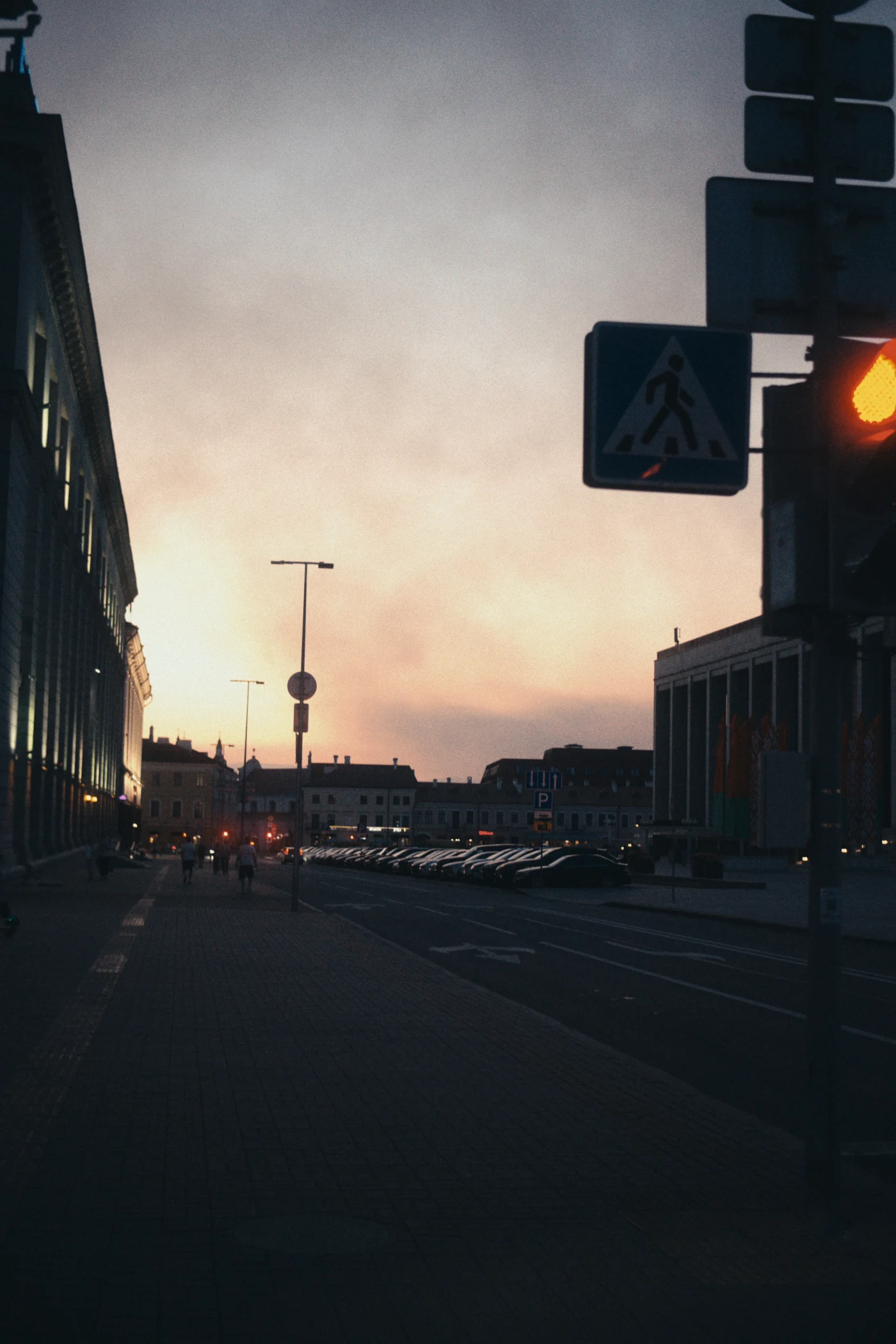 A street at sunset, with a traffic light showing red and buildings on both sides of the road.