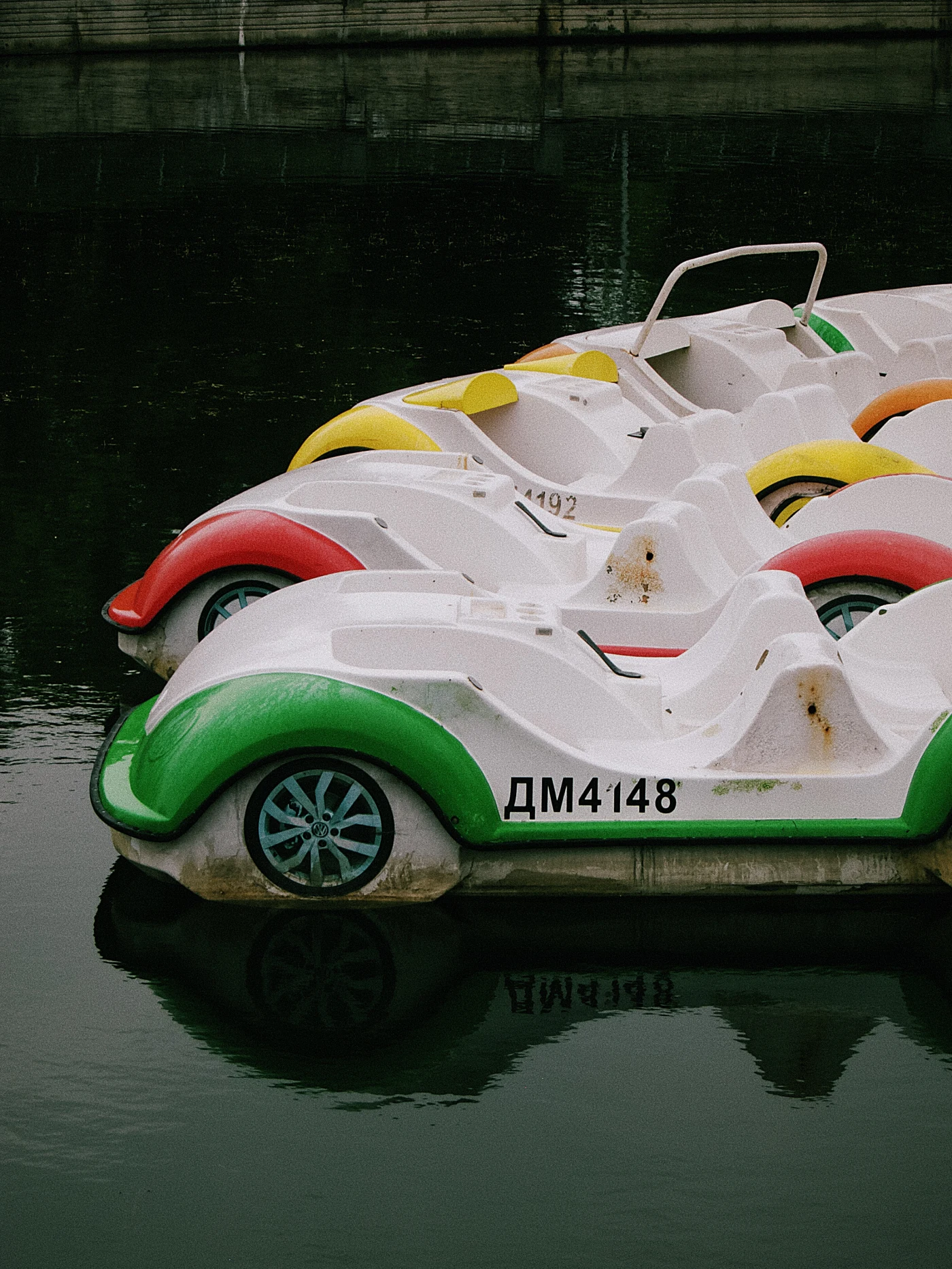 Pedal boats on the water, painted yellow, red and green, reflected in the calm water.