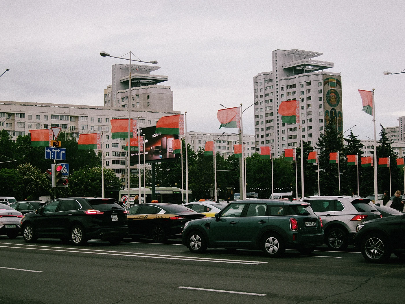 A street with cars and flags, with multi-story buildings and billboards in the background.