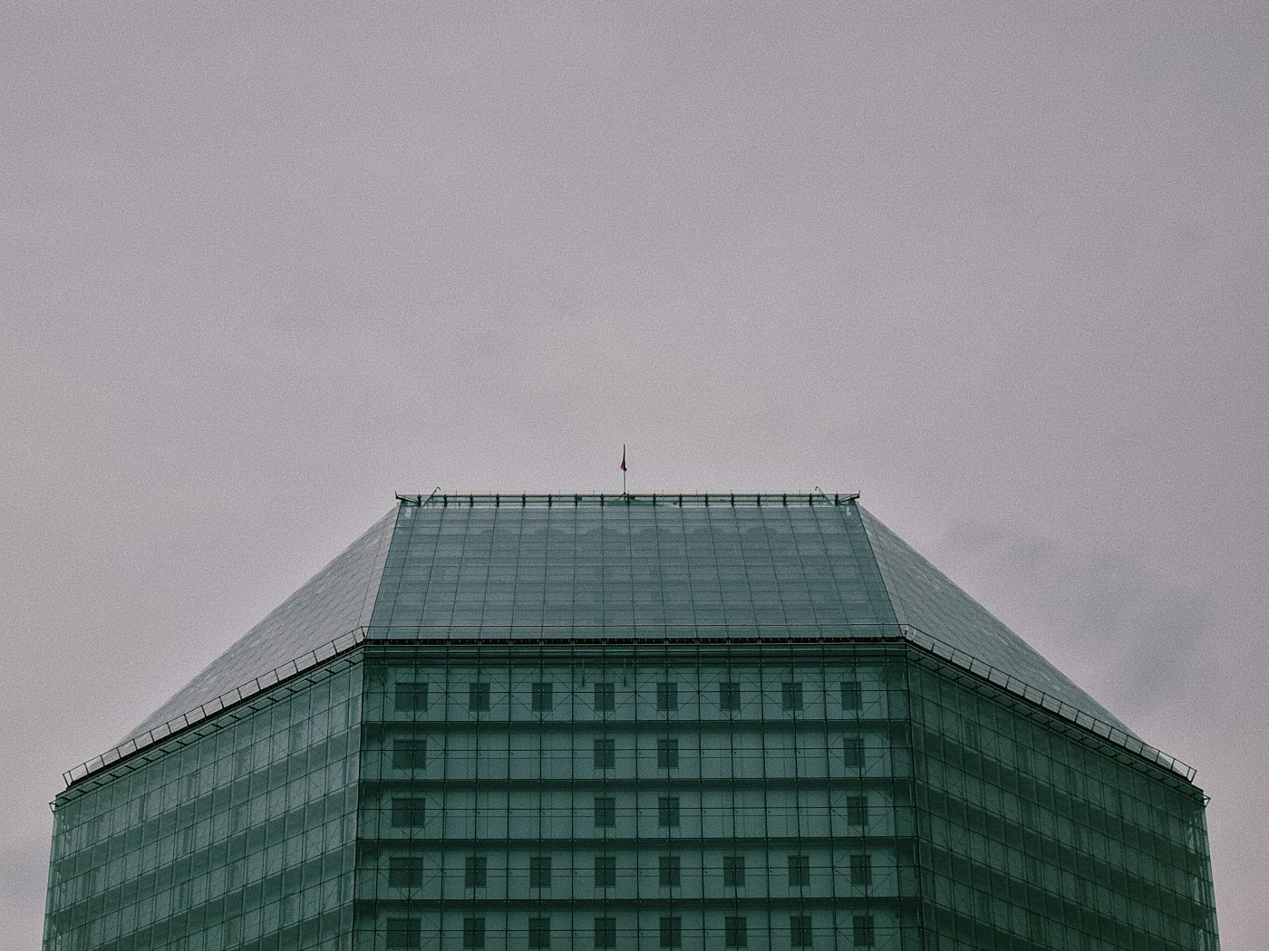 A glass building with a pyramidal roof against a gray sky.