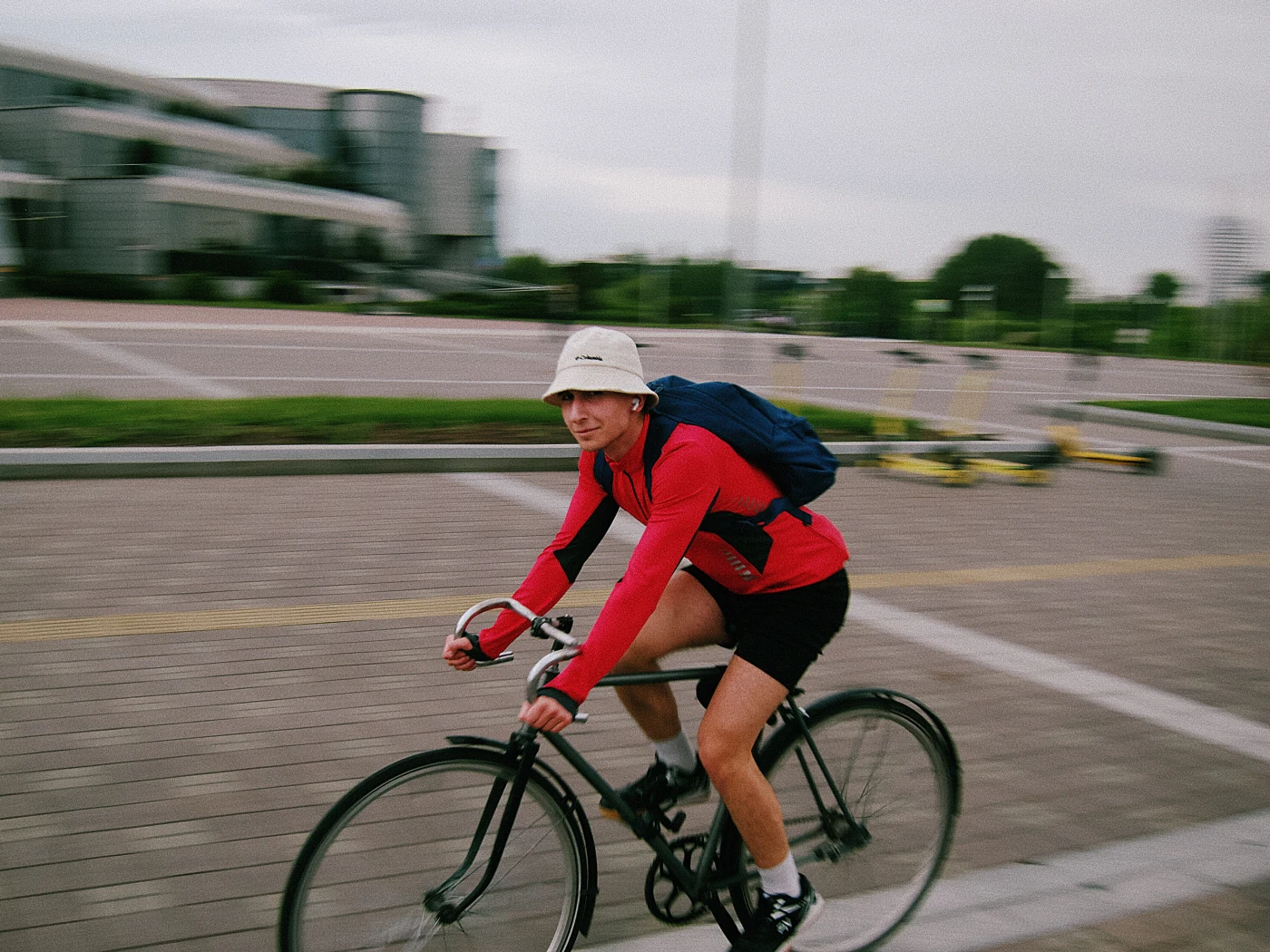 A guy in a red T-shirt and white hat rides a bicycle along an asphalt path.