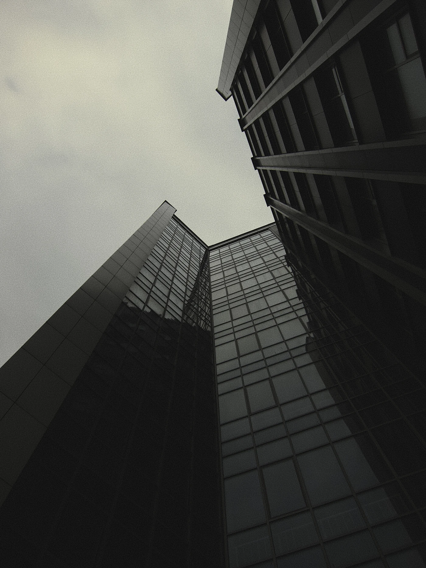 High-rise buildings with reflections in the glass, gray sky. The shot is taken from below.
