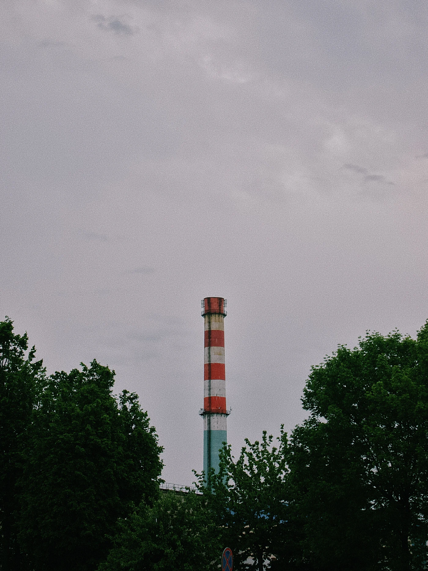 A smokestack with red and white stripes against a cloudy sky and green trees.