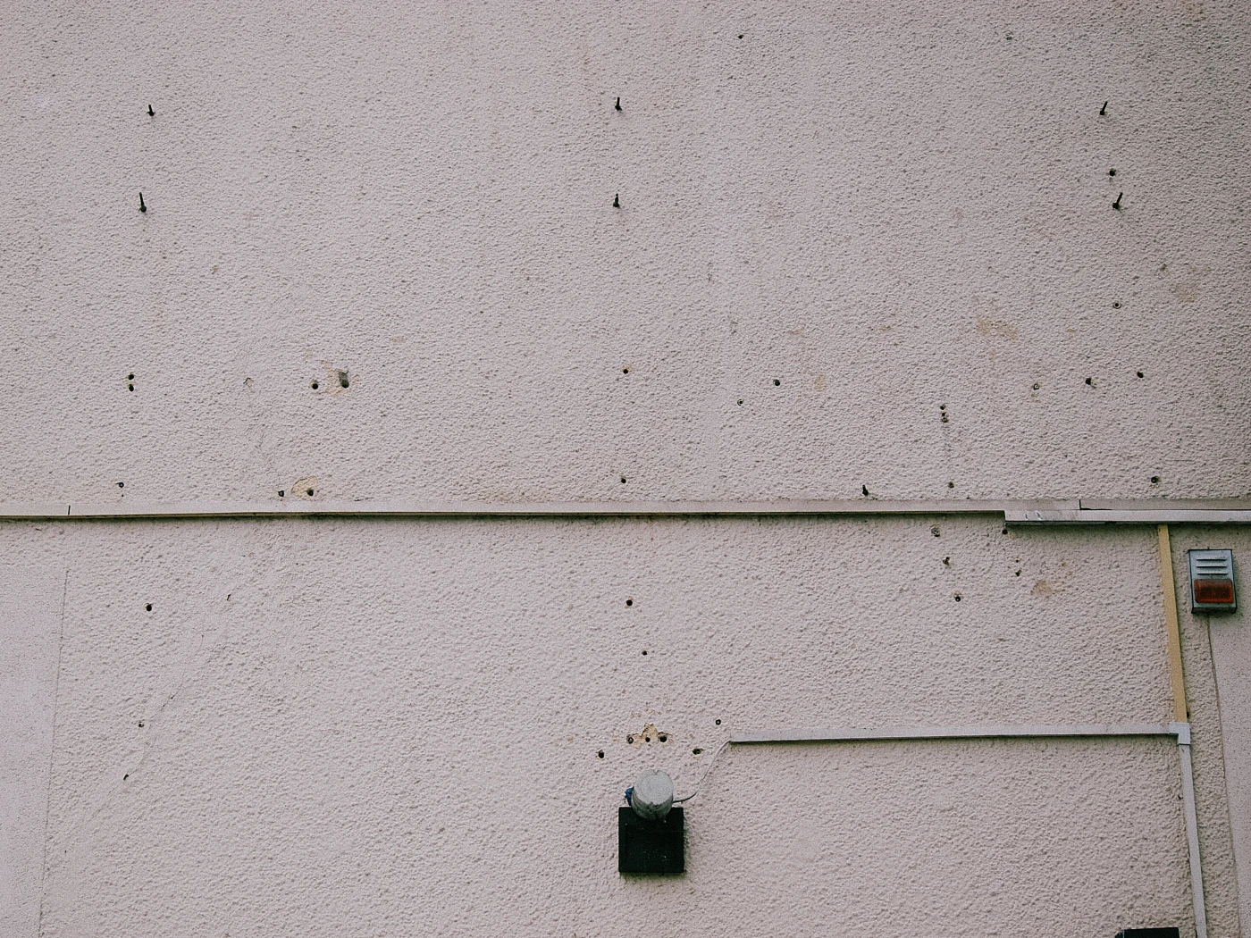 A gray wall with small holes and wires, with a round light fixture mounted on it.