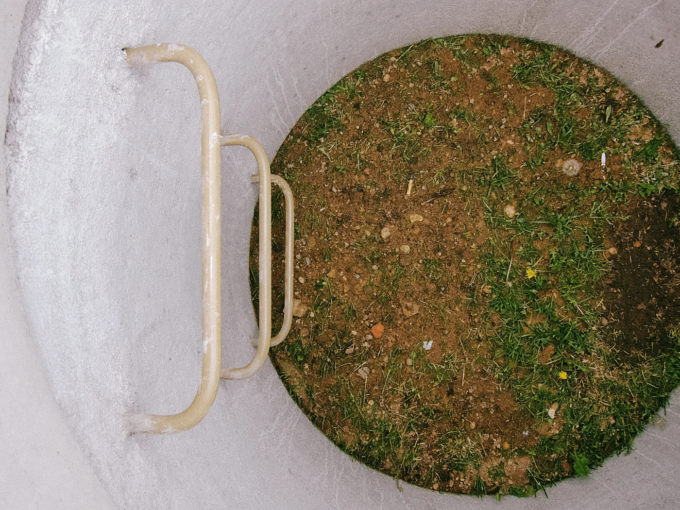 A round well with a metal handle, with soil and grass visible at the bottom.