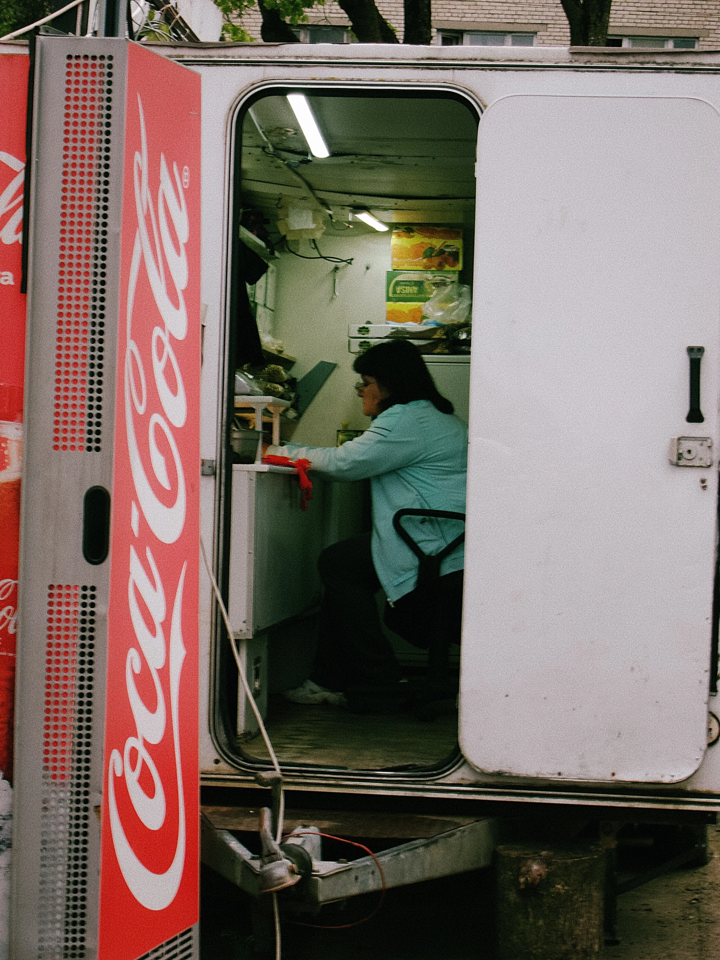 A woman sits in a van with a Coca-Cola logo, selling food or drinks.