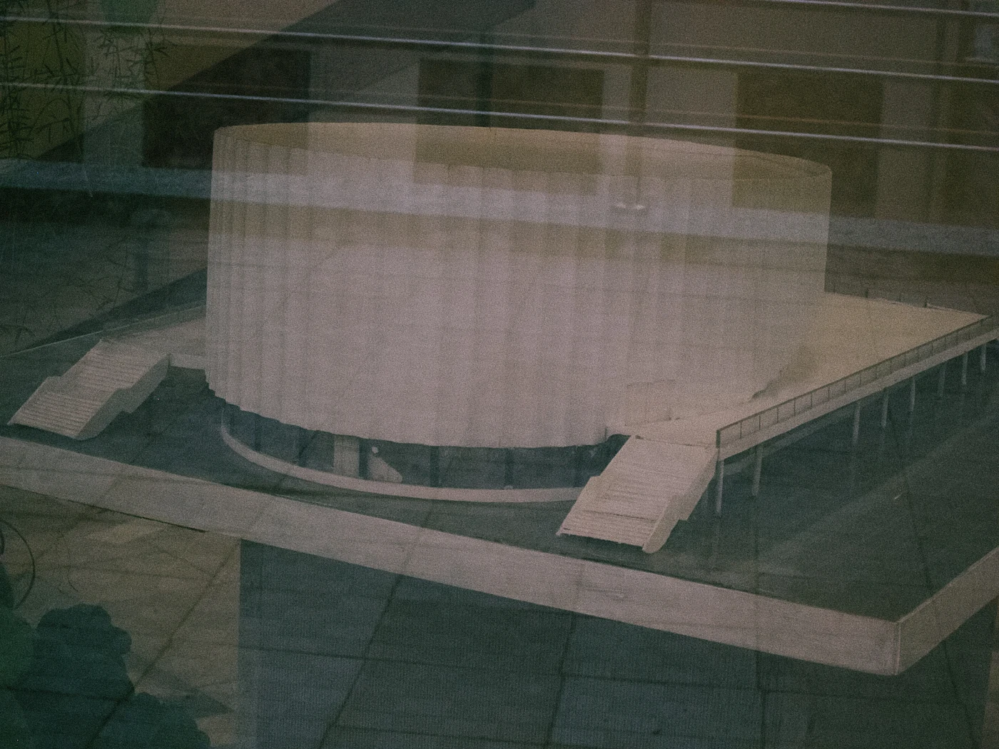 A model of a round building with stairs, reflected in glass.
