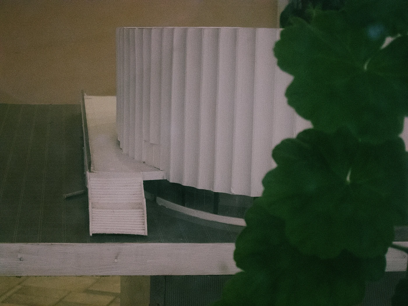 A model of a building with a wavy facade wall, placed on a table next to a green plant.