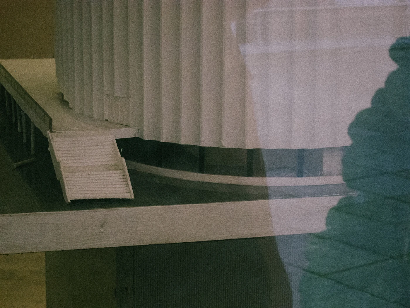 A model of a building with a ribbed wall and a slanted staircase, reflected in glass.