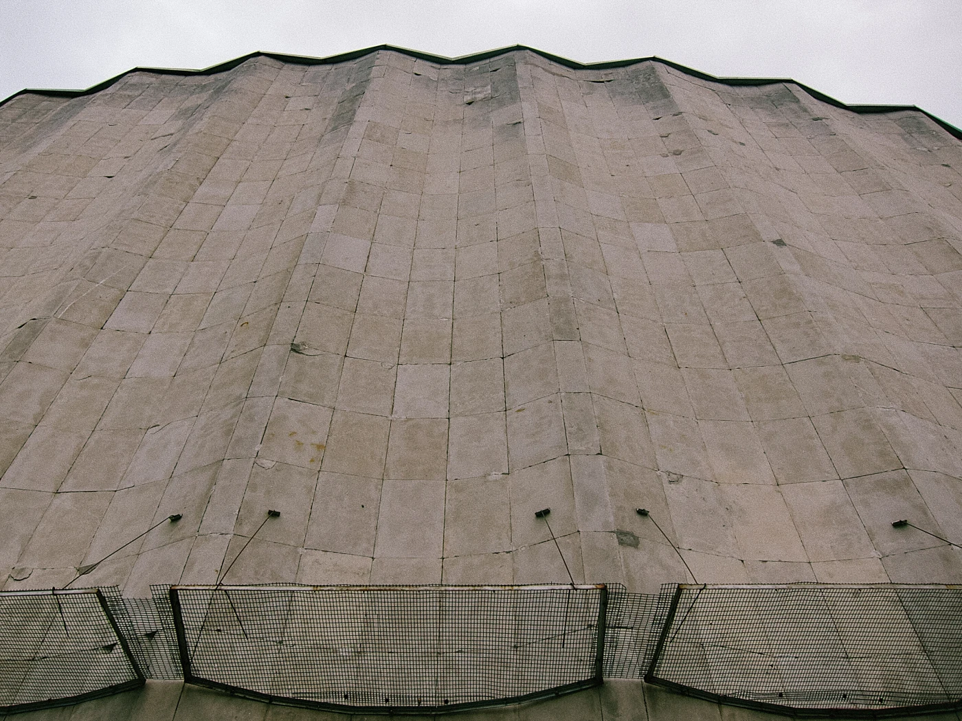 A building facade with a wavelike texture, gray in color, with a mesh in the foreground. Cloudy weather.