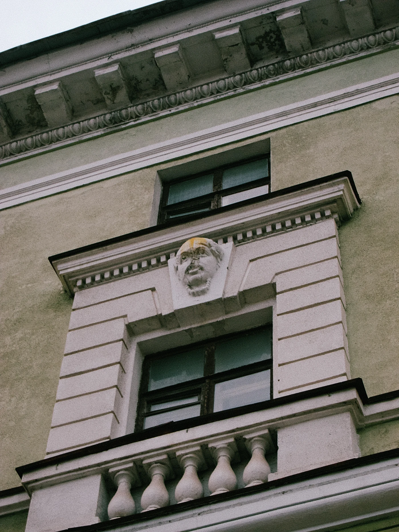 A fragment of a building facade with an architectural element shaped like a face above a window.