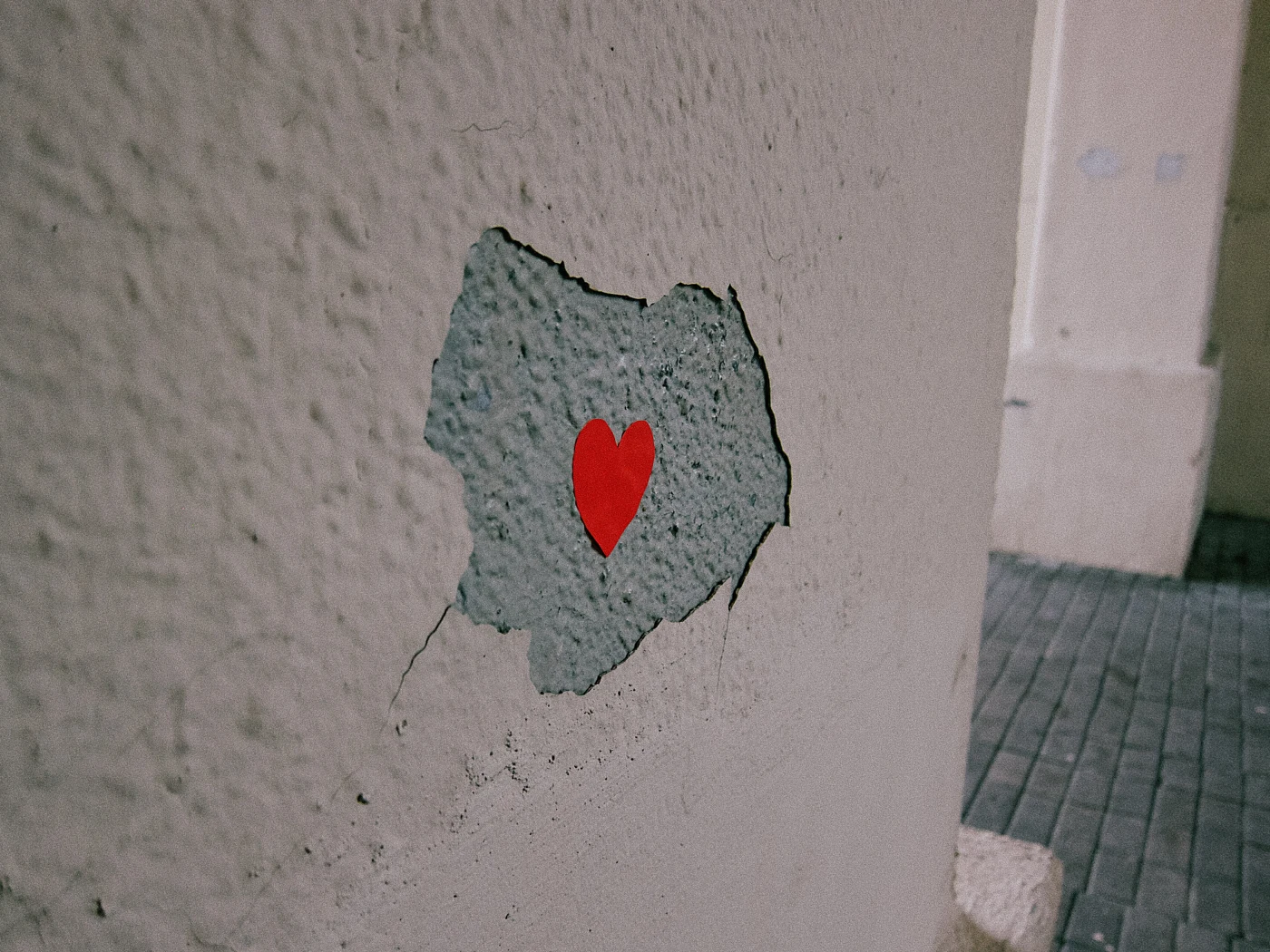 A crack in the wall with a red heart-shaped sticker.