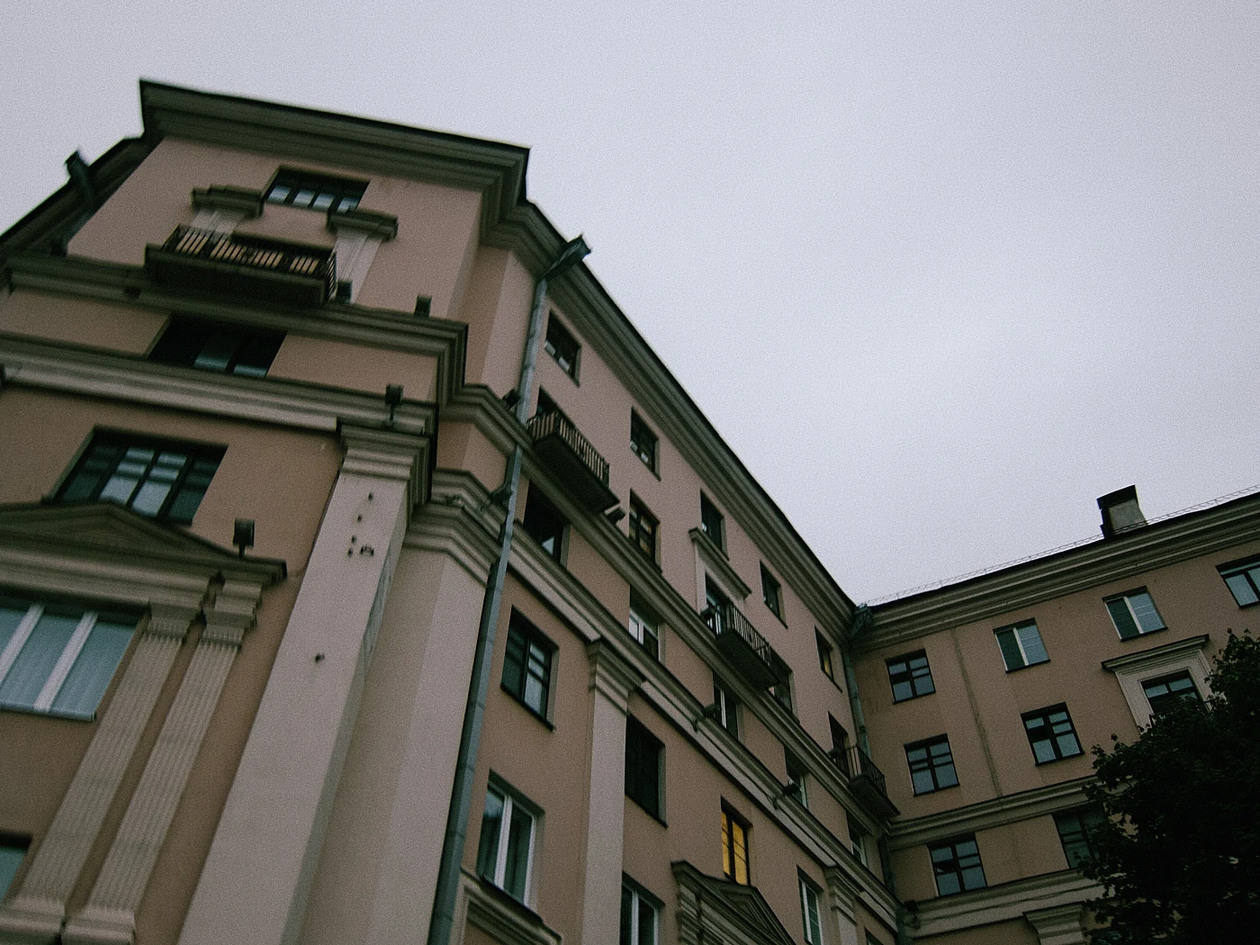 A building facade with balconies, windows and a gray sky in the background. One of the windows is lit.