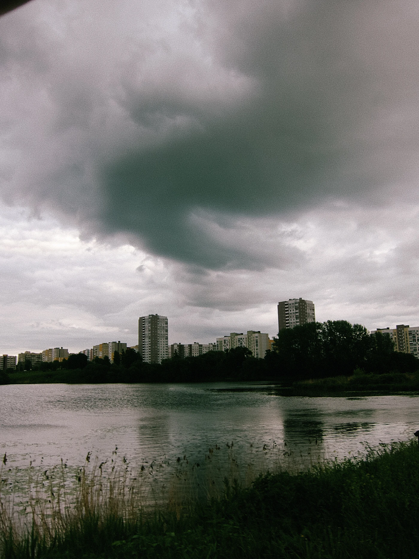 Темное облако над городом, отражение в воде, серое небо, здания на фоне.
