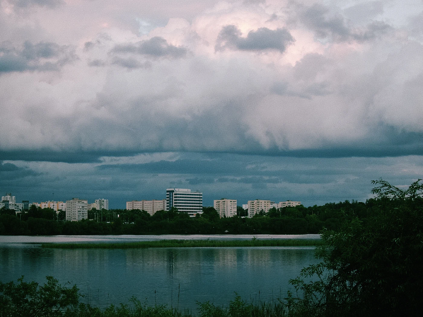 Городской пейзаж с облачным небом и отражением в воде, на фоне жилых зданий.