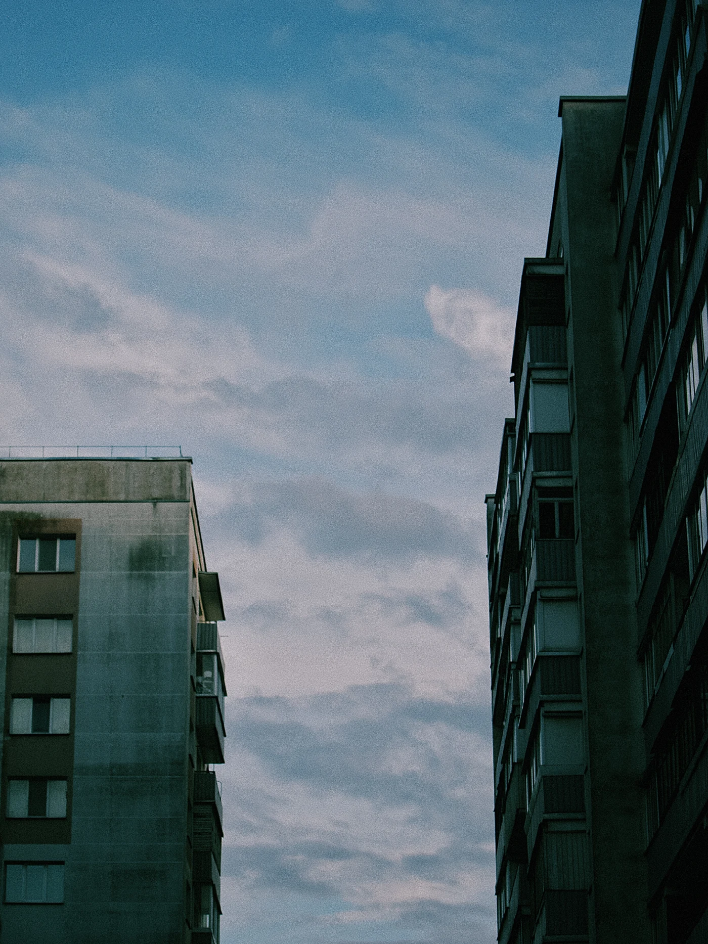 Two buildings against a blue sky with clouds.