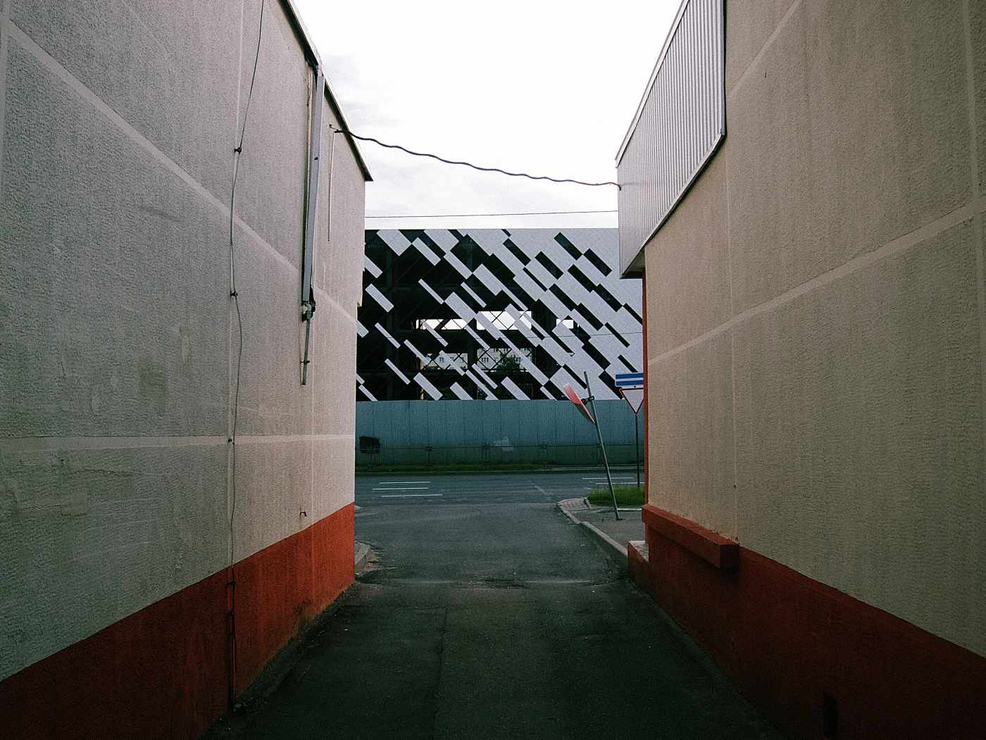 A narrow passage between buildings with a view of a modern facade with black-and-white geometric patterns.