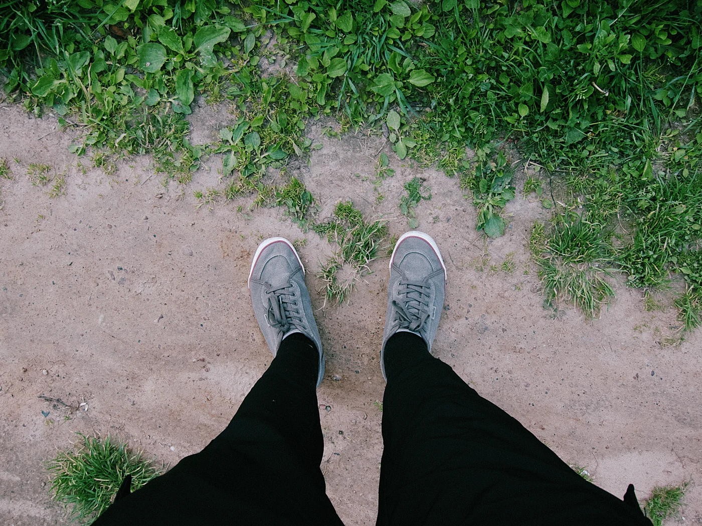 Feet in gray sneakers on a path surrounded by green grass.