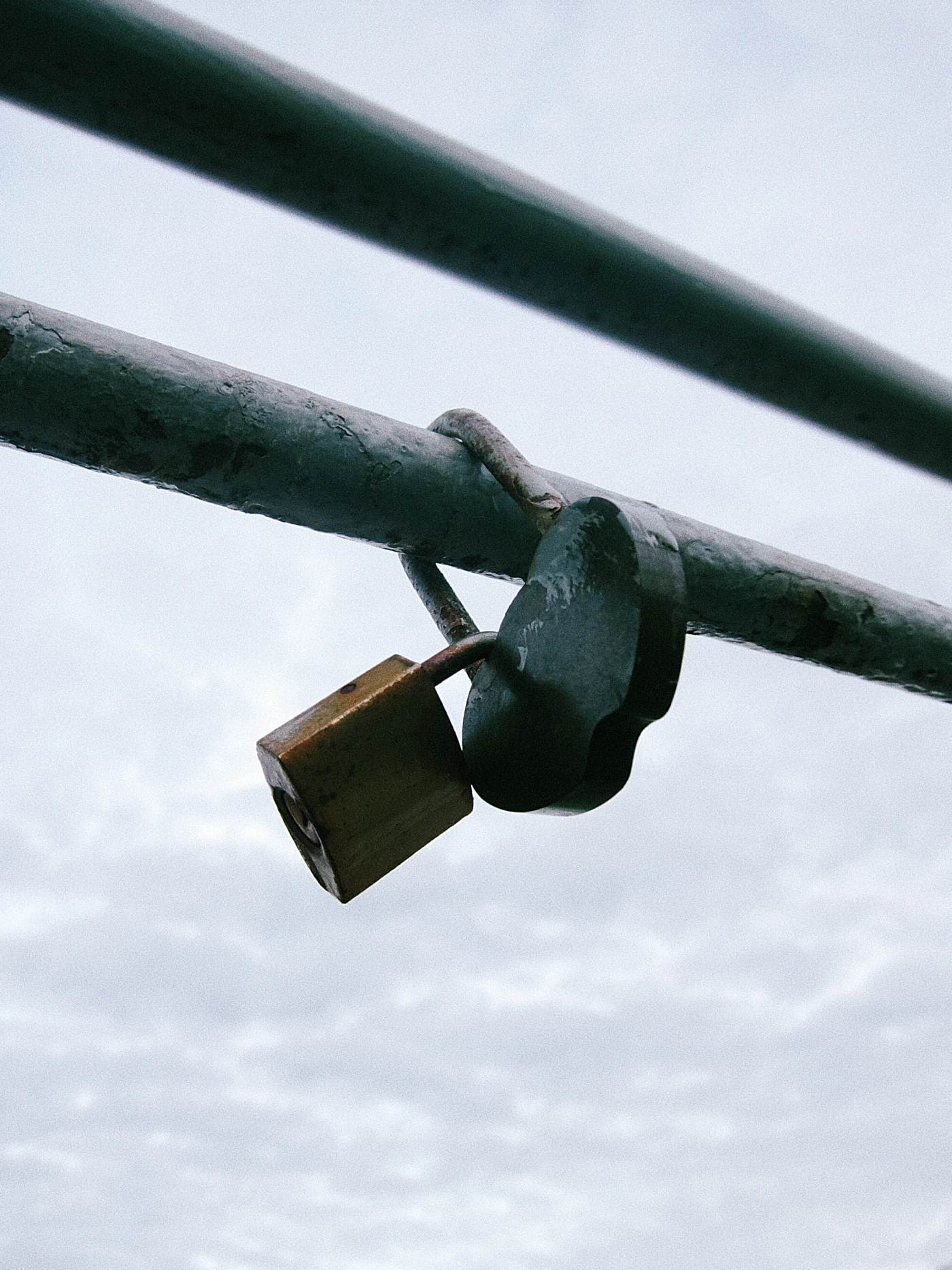 A padlock on a metal crossbar against a cloudy sky.