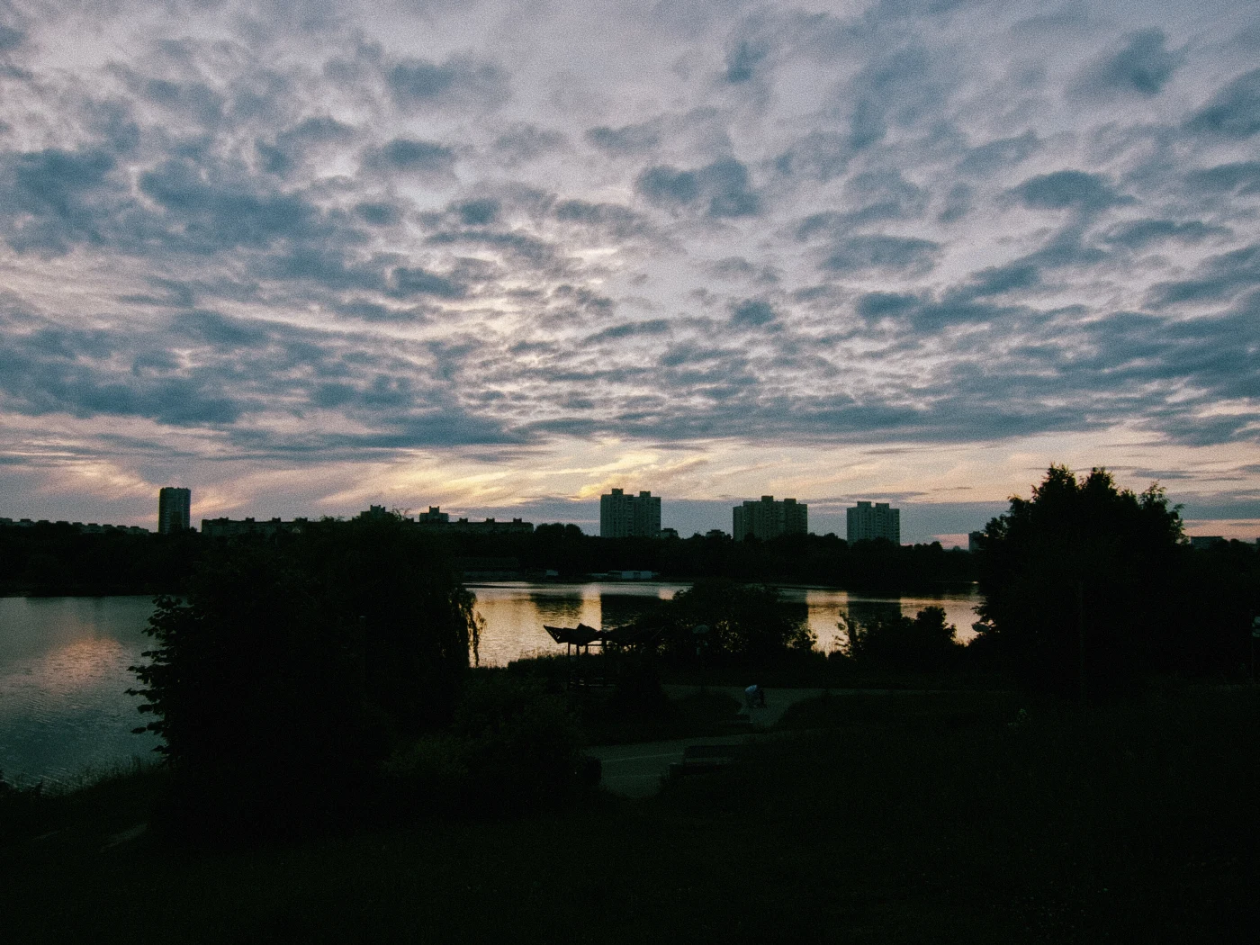Sunset over the river, clouds in the sky, silhouettes of buildings against the water.