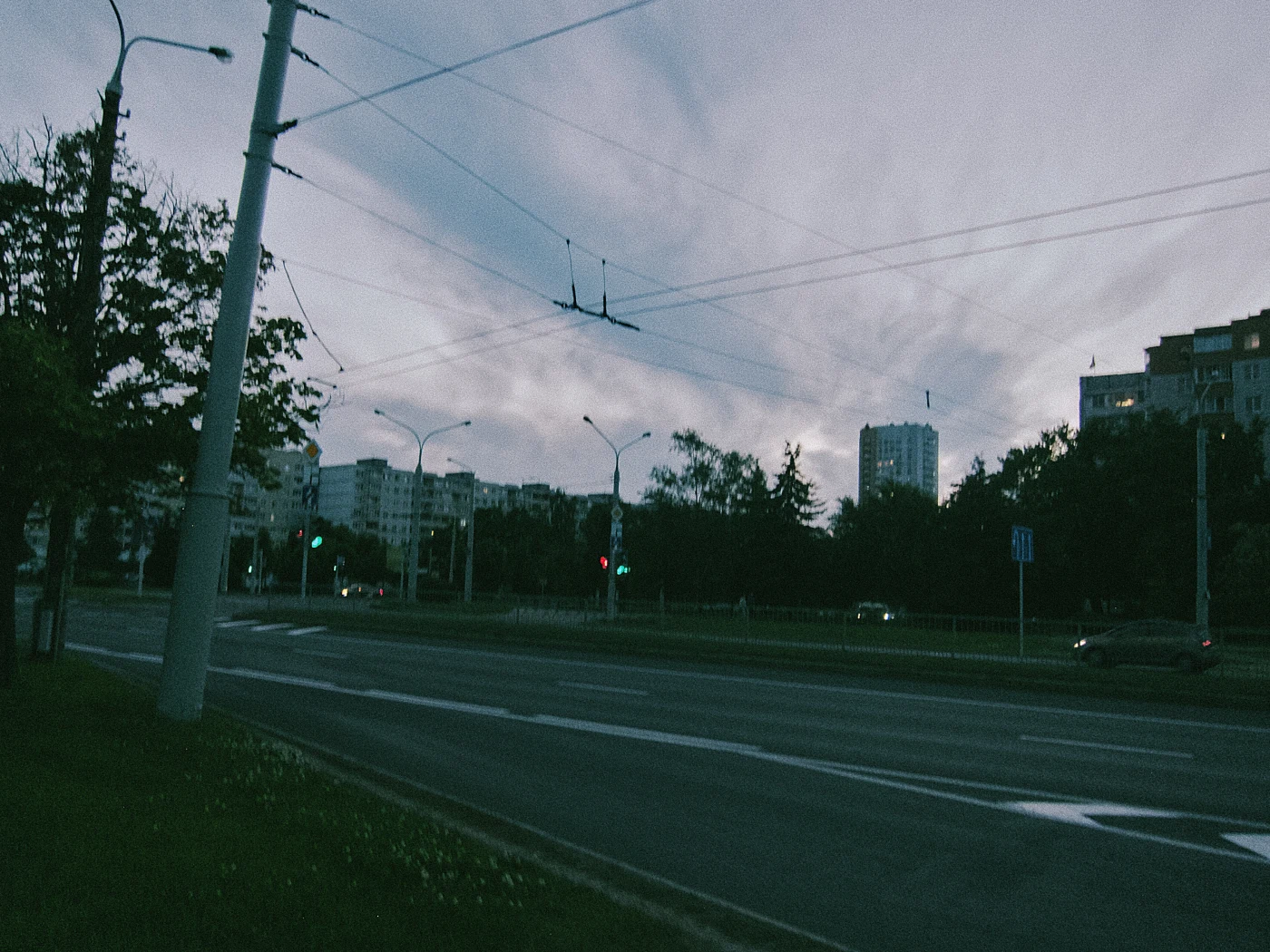 A street with a green traffic light, buildings against an evening sky with clouds.