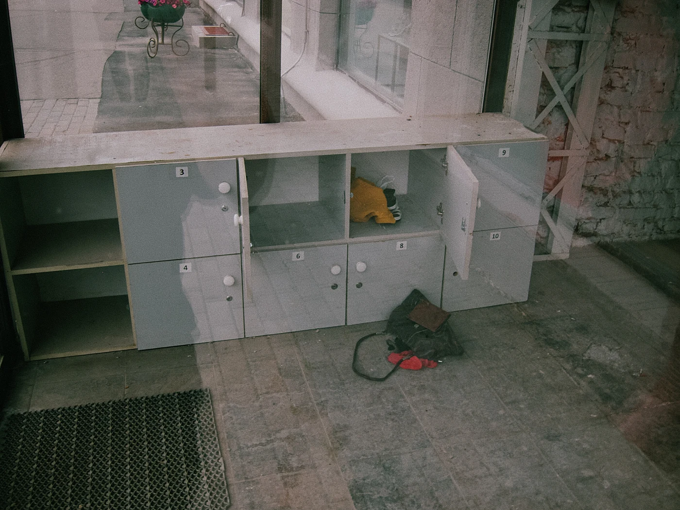 An empty cabinet with drawers and open doors, with tools and a mat lying on the floor.