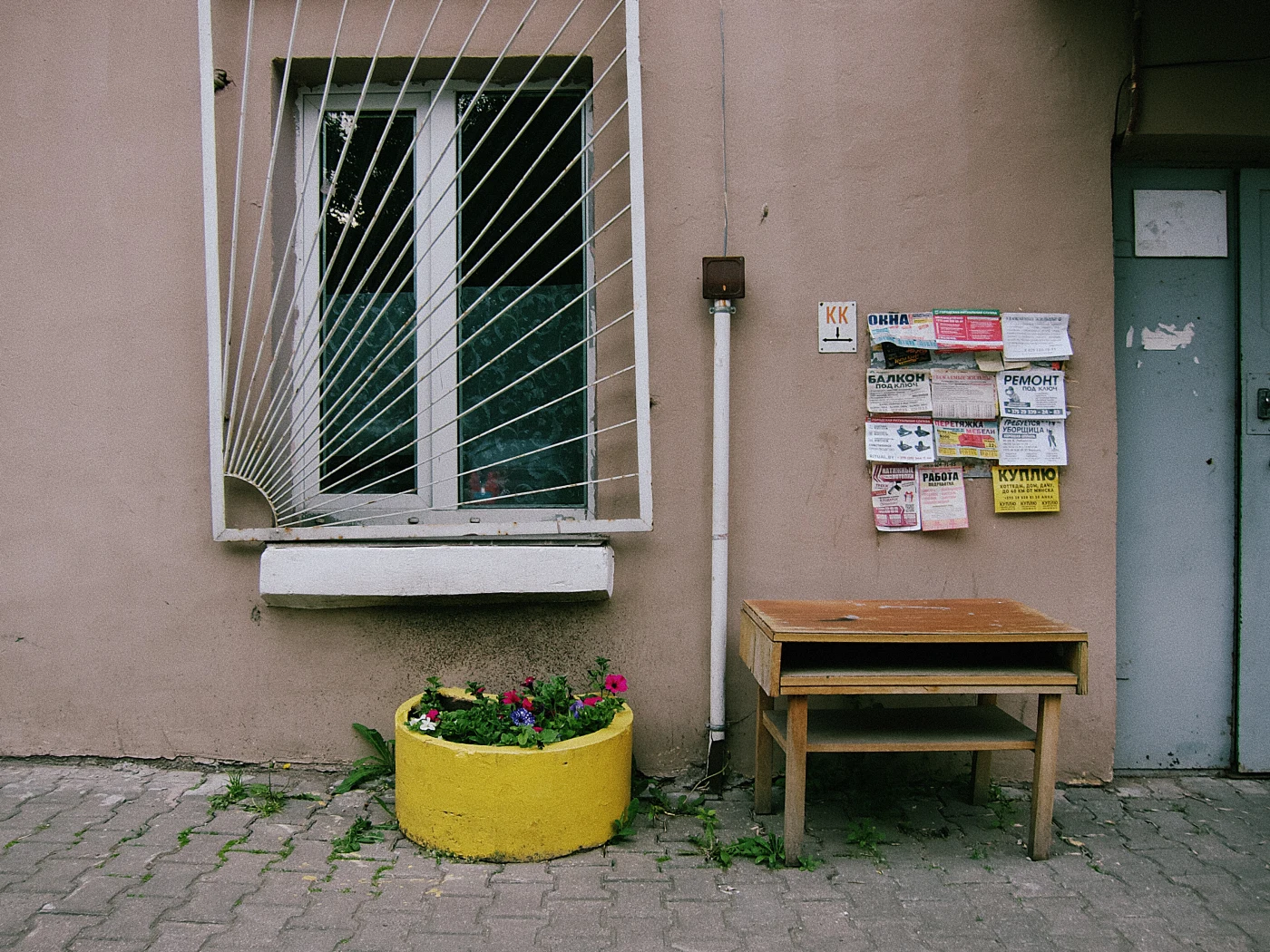 A yellow flower bed, a table, and a notice board by the wall of a house.