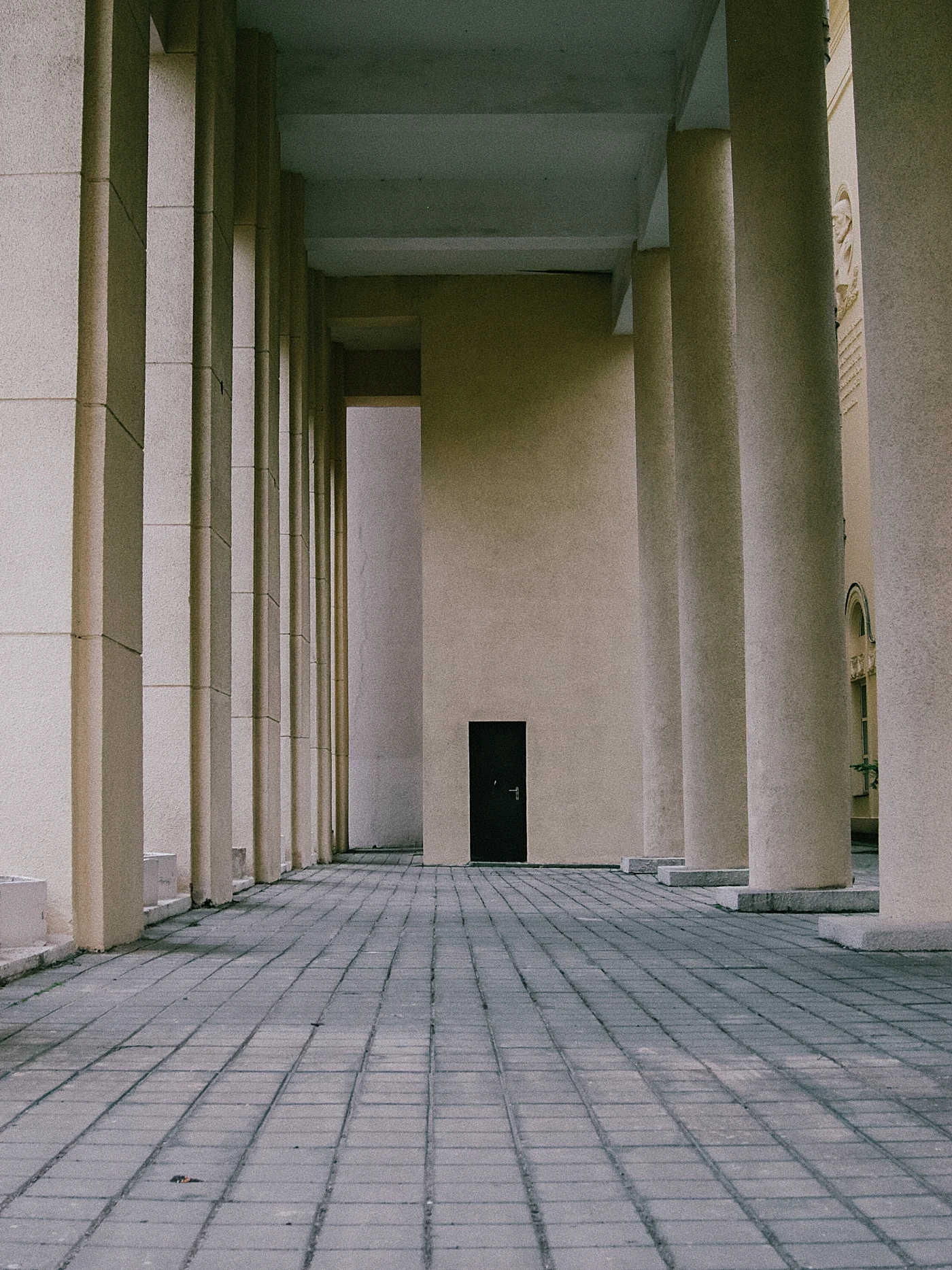 An empty corridor with columns and a door at the end, creating an atmosphere of mystery and solitude.