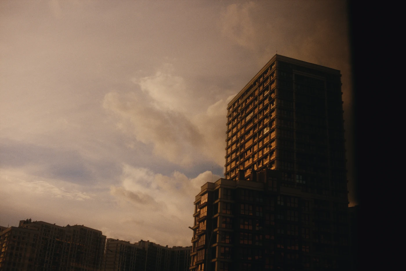 A high-rise building against a cloudy sunset sky. Warm light reflects in the windows.