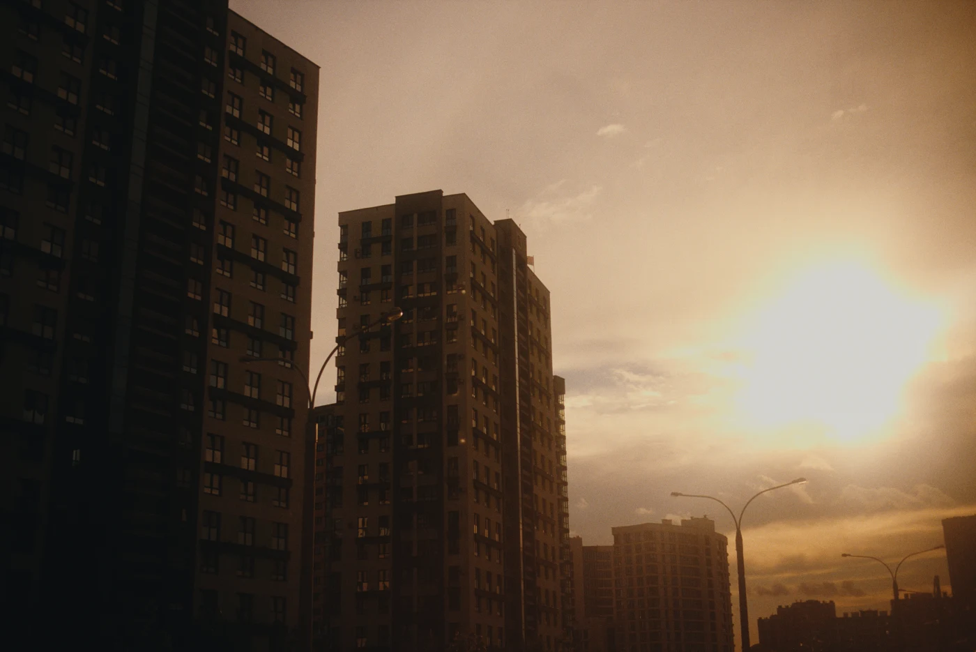 Silhouettes of high-rise buildings against the sunset, with bright rays of sunlight illuminating the clouds.