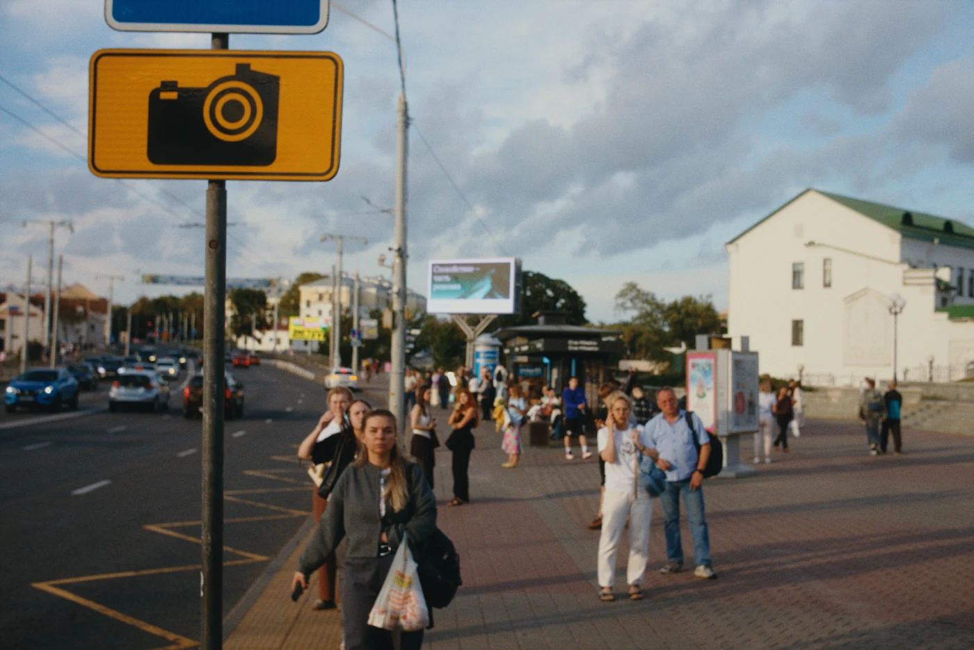 A busy street with many people, road signs, and billboards. Sunny weather with clouds in the sky.