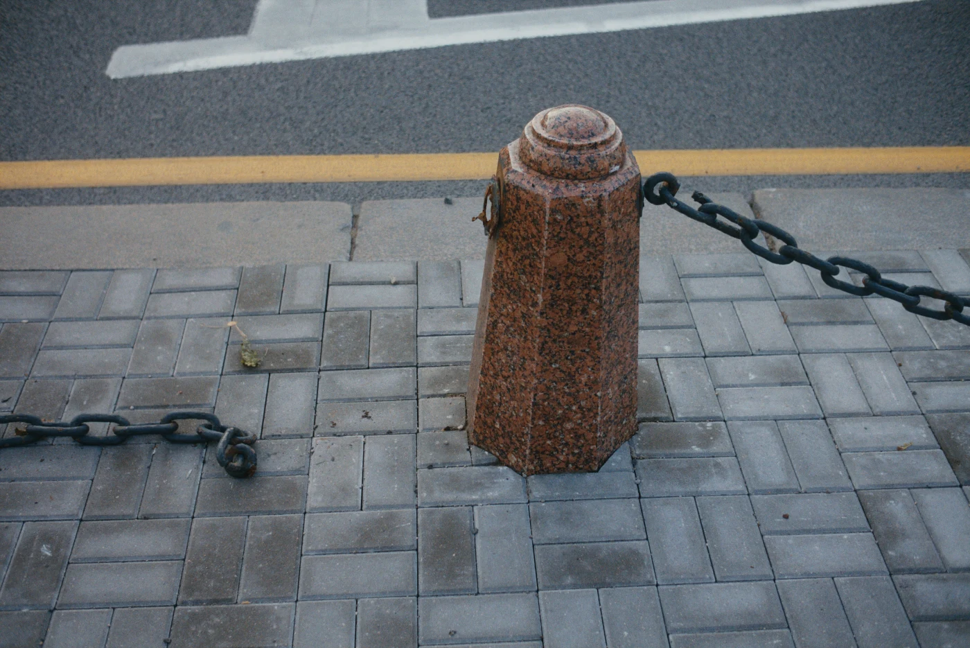 A stone post with a chain on the sidewalk beside the roadway.