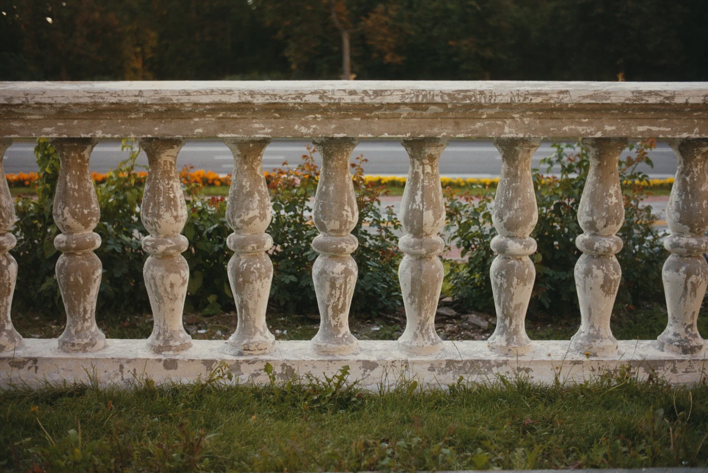 An old white balustrade with worn surfaces against greenery and flowering plants.