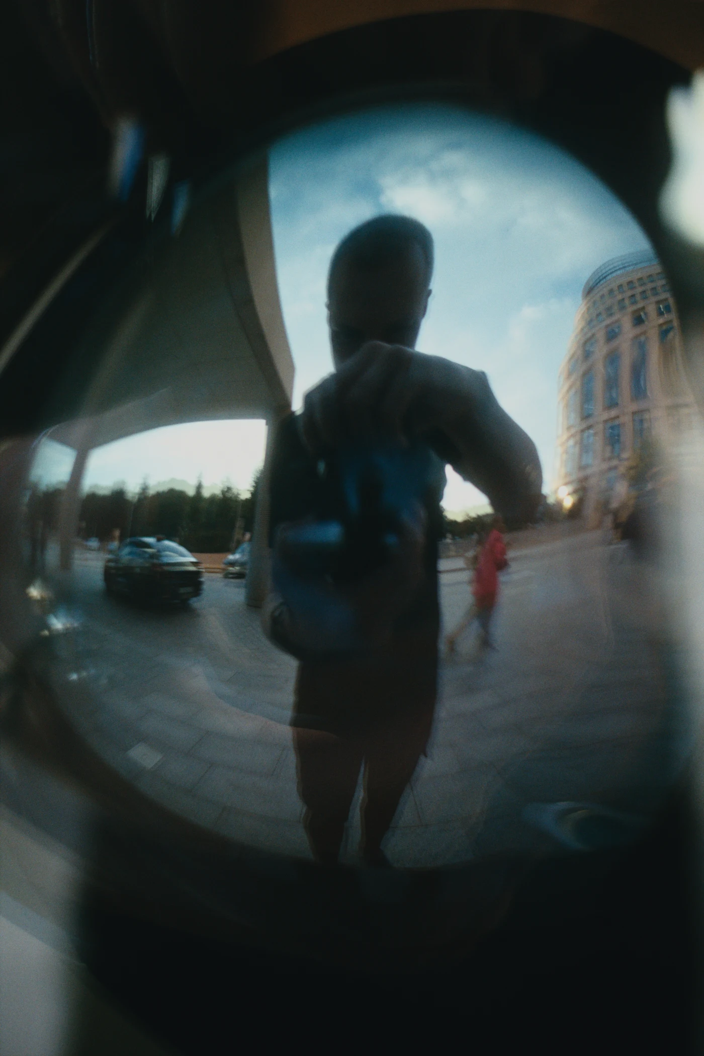 A reflection of a person with a camera in glass, with a city street and buildings in the background.