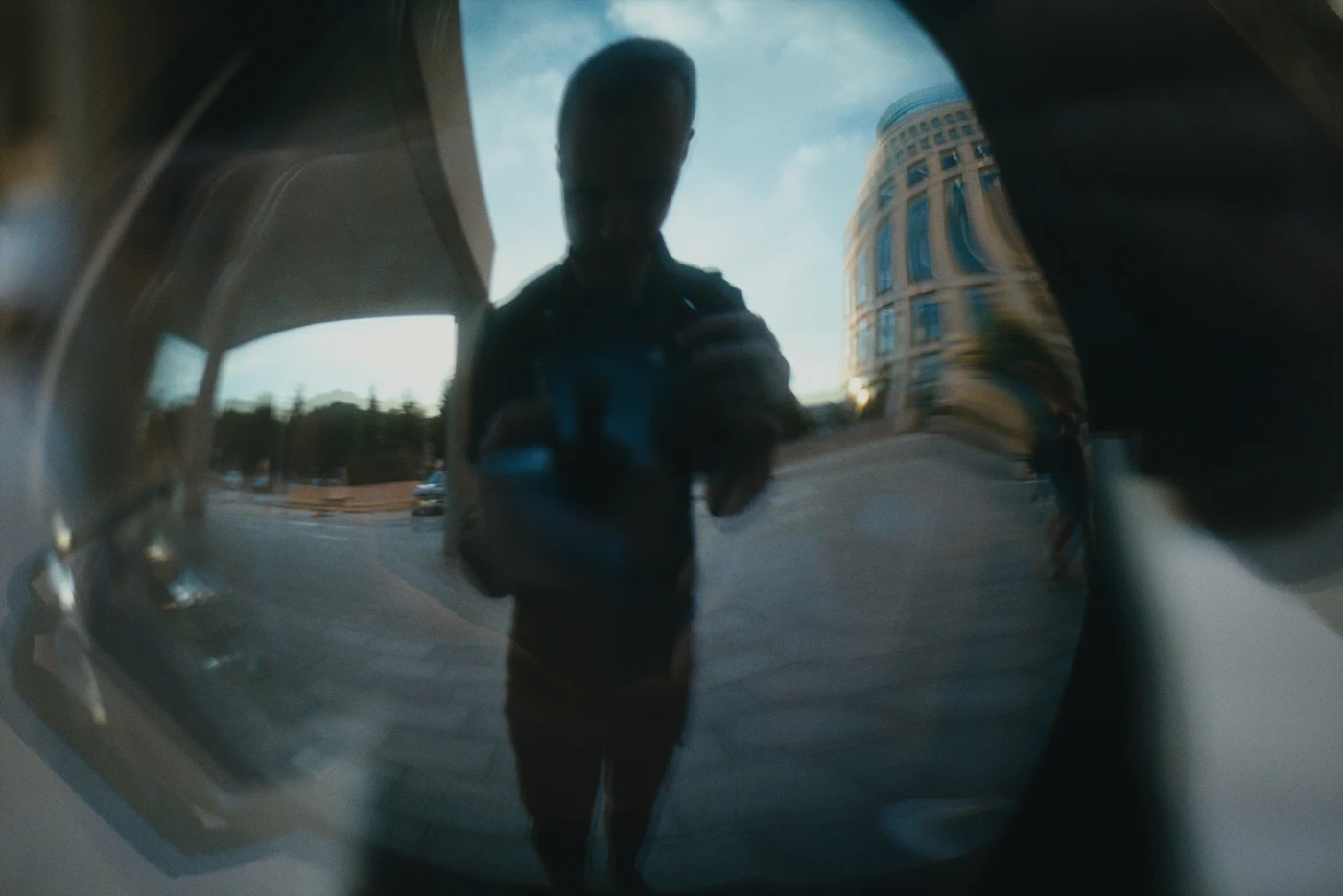 A reflection of a person in a metallic surface, with buildings and sky in the background.