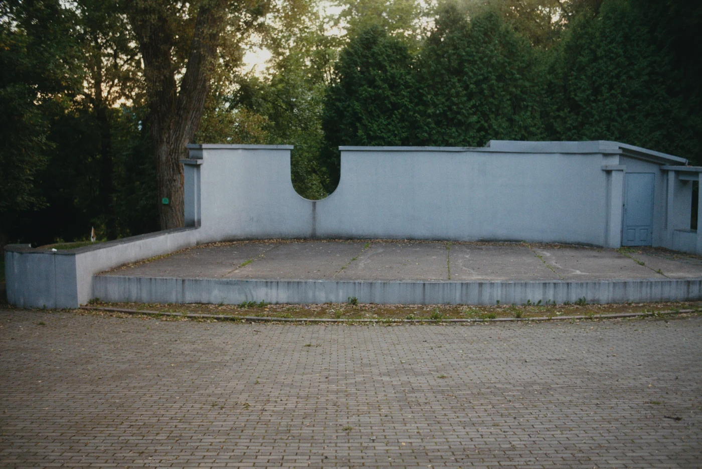 An empty area with gray walls and green trees in the background, with no objects or people.
