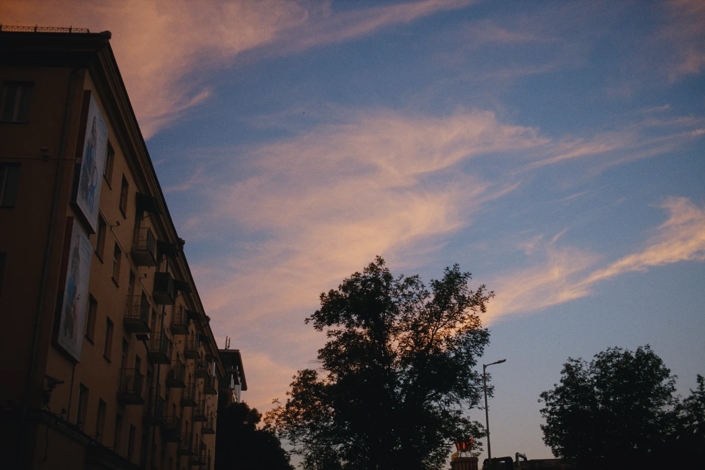 A sunset sky with clouds above a building and trees in the foreground.