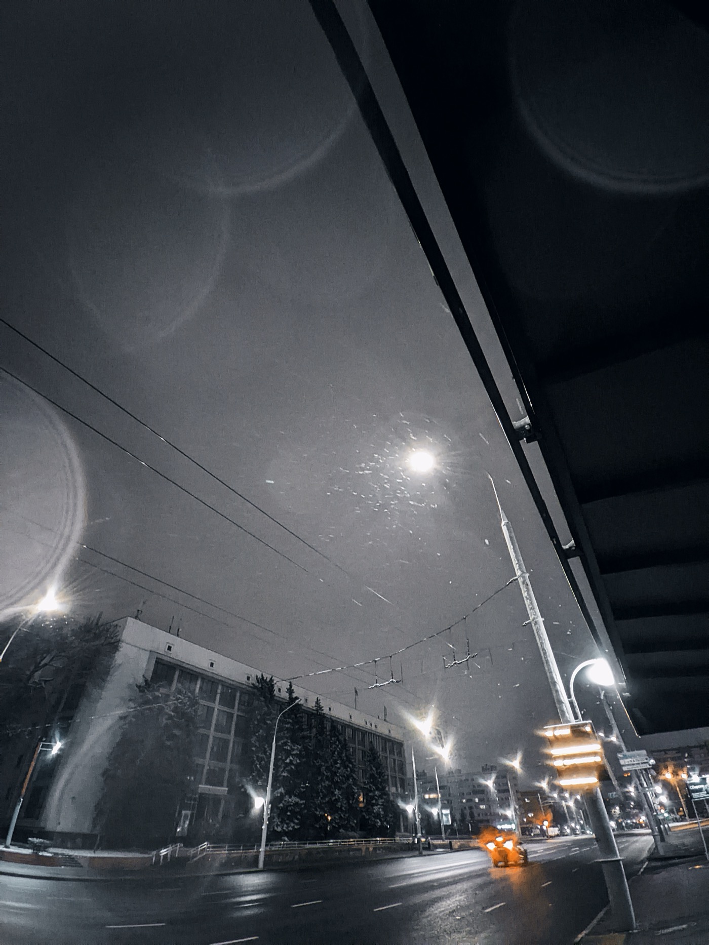 Ночной городской пейзаж с улицей, освещенной фонарями, и луной на небе. Снег падает, создавая атмосферу зимы.