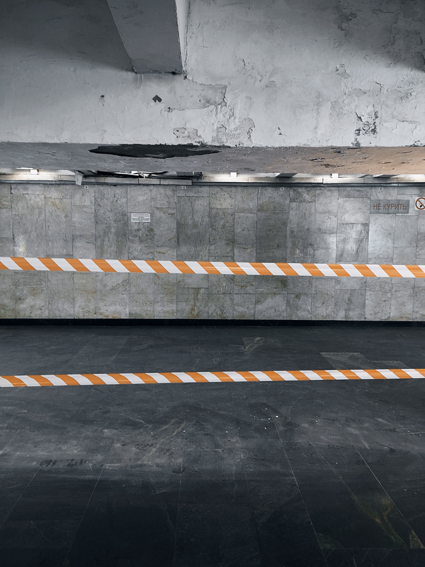 Пустое помещение с серыми стенами и оранжево-белой лентой, предупреждающей о запрете прохода.