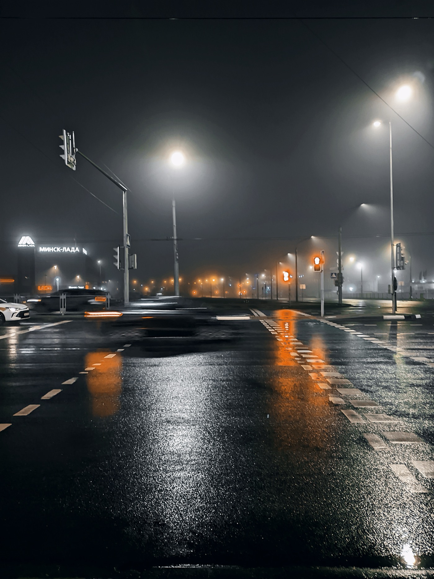 Ночной перекресток с размытой видимостью, светофоры и отражения на мокрой дороге.