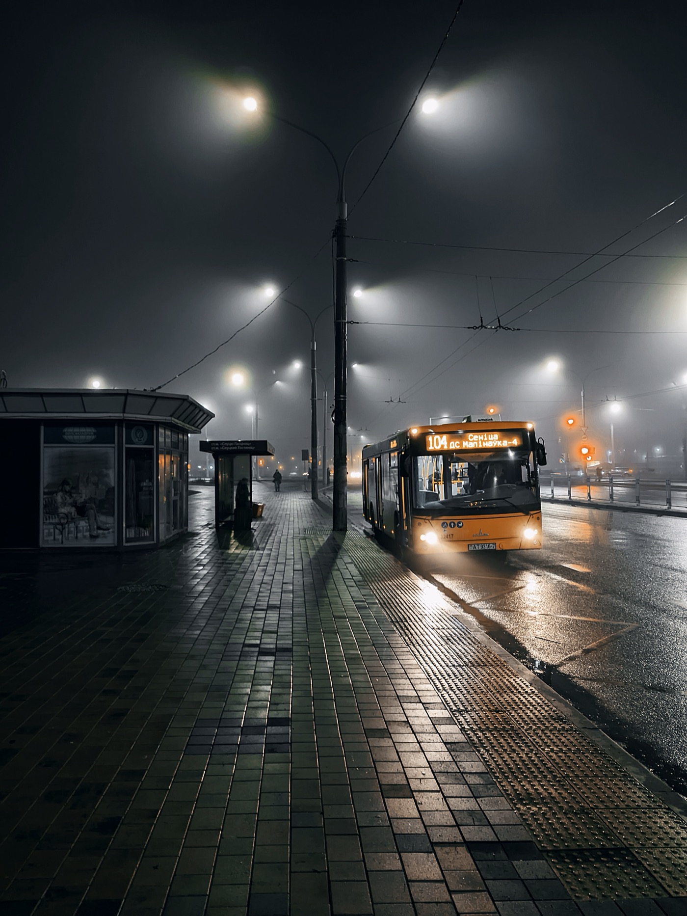 Ночной городской пейзаж с автобусом 104 на остановке, освещённый фонарями в тумане.