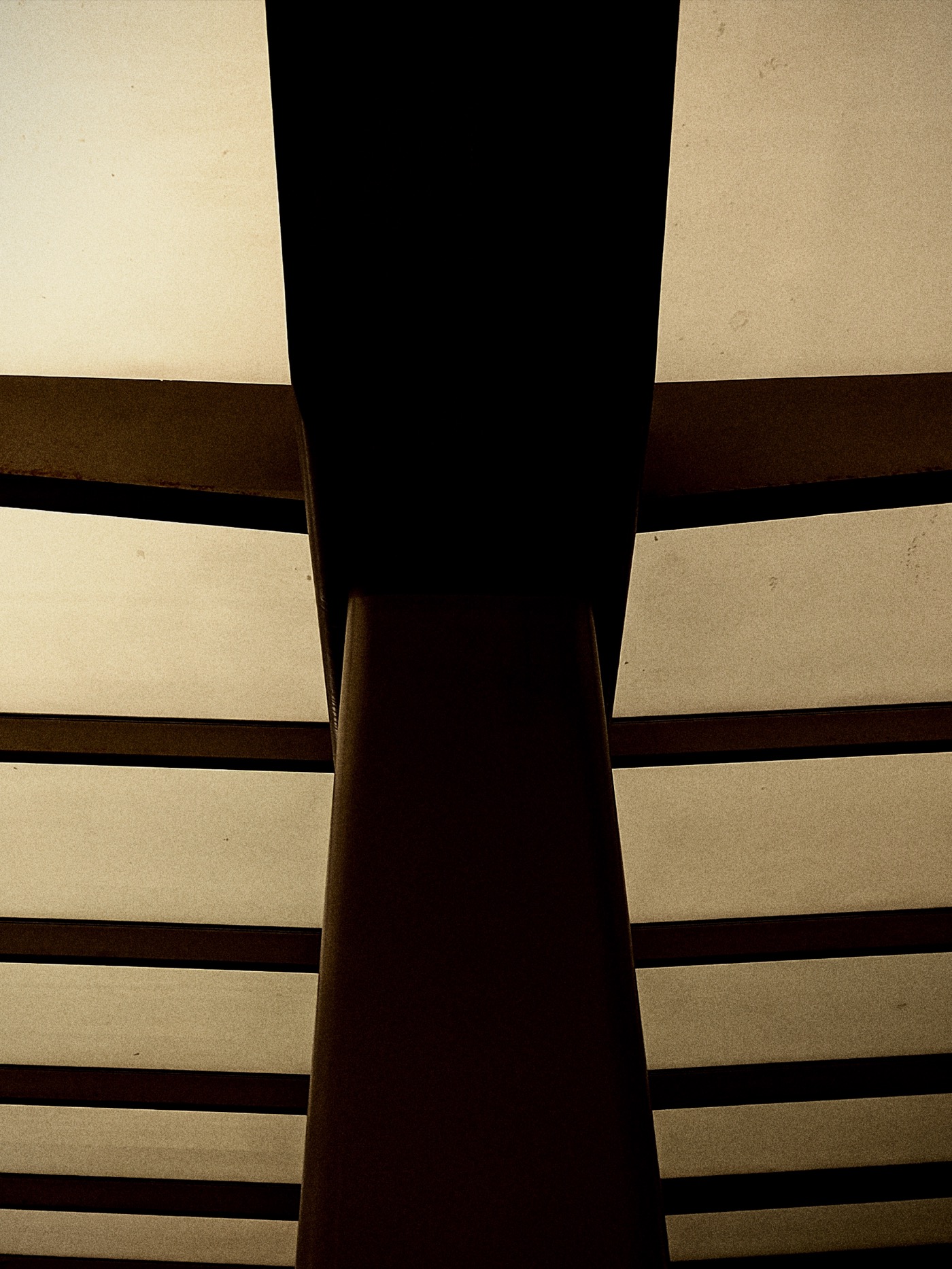 Чёрная колонна на фоне светлого потолка с горизонтальными перекрытиями.