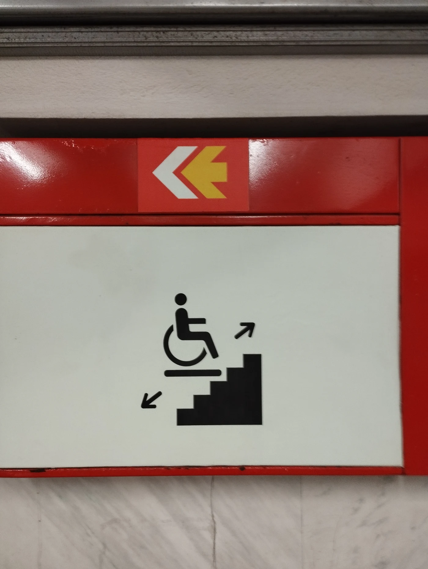 A sign showing a person in a wheelchair, with arrows pointing toward a staircase and an exit.