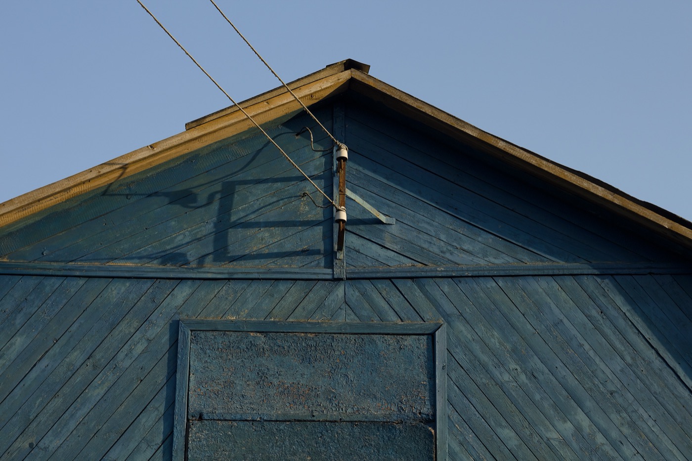 Синий дом с деревянной отделкой и крышей, на фоне ясного неба. Провода тянутся вдоль крыши.